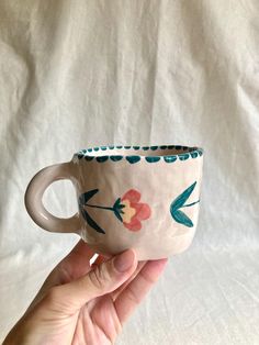 a hand holding a coffee cup with floral designs on the outside and inside, in front of a white background