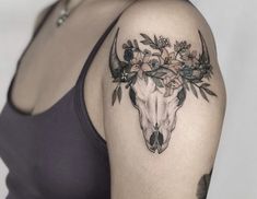 a woman's arm with flowers and a bull skull tattoo on her left shoulder