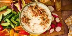 a bowl of dip surrounded by vegetables on a cutting board with chips and crackers