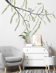 a living room with a chair, dresser and tree branch wall decal on the wall