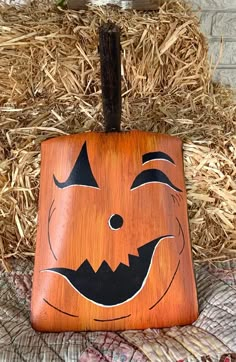 a wooden square with a carved pumpkin face on it's side and hay in the background