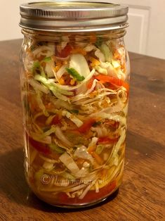 a glass jar filled with assorted veggies on top of a wooden table