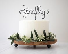 a white cake topped with greenery on top of a wooden stand