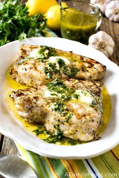 two pieces of chicken on a plate with lemons and parsley in the background