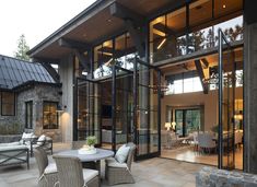 a patio with chairs and tables in front of a large glass doored entrance to a house