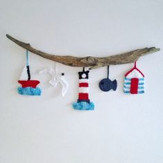 three knitted ornaments hanging from a branch on a white wall next to a piece of driftwood