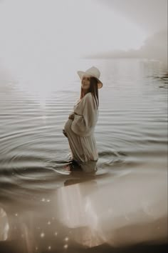 a woman in a white dress and hat standing in the water with her hands on her hips