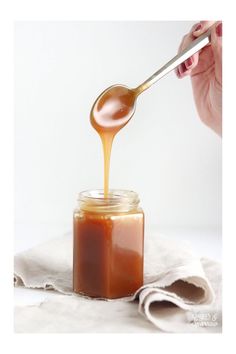 a woman spooning honey into a jar on a napkin with a white cloth underneath