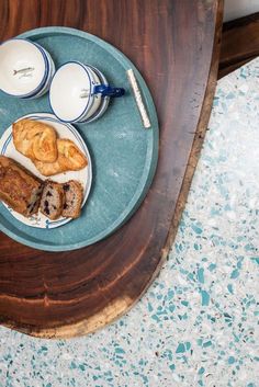 a blue plate topped with pastries on top of a wooden table next to two cups