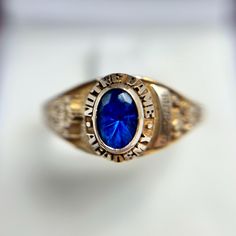 This Vintage 10K Yellow Gold Notre Dame Academy Class Ring features a striking blue oval gemstone at its center, symbolizing school pride and achievement. The gemstone is encircled by the words "Notre Dame Academy," adding a distinguished touch to this classic design. Crafted in 10K yellow gold, the ring showcases intricate detailing on the shank, including school insignias and personalized engravings, reflecting the wearer's connection to their alma mater. With a ring size of 8.25 and a band width of 1.8mm, this ring is both substantial and comfortable, weighing 4.57 grams. This piece is not only a meaningful keepsake but also a timeless piece of jewelry that carries the legacy of a cherished educational institution. School Pride, Alma Mater, Rings Statement, Timeless Pieces, Notre Dame, Class Ring, Statement Rings, Classic Design, Jewelry Rings