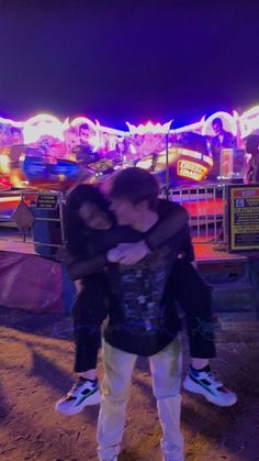 two people hugging each other in front of an amusement park at night with neon lights