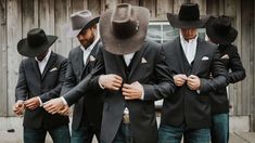 a group of men wearing hats standing next to each other in front of a barn