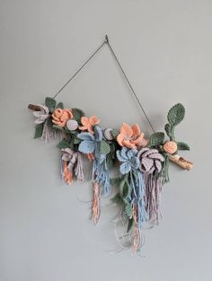 a wall hanging made out of yarn with flowers and leaves attached to the side of it