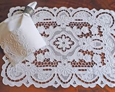 a white doily on a wooden table with a napkin in the middle and an embroidered ring resting on it