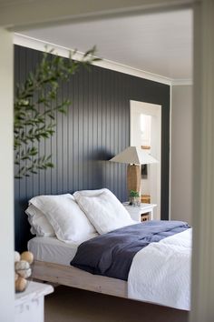 a bed with white and blue sheets in a bedroom next to a plant on the wall