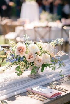 a vase filled with white and pink flowers sitting on top of a table next to silverware