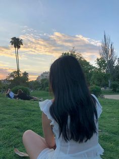 a woman sitting in the grass with her back to the camera, looking at something