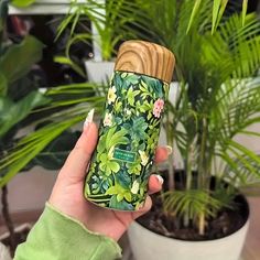 a woman holding up a green lighter in front of a potted plant with leaves and flowers on it