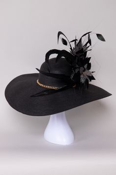 The Pure Elegance Derby Hat embodies timeless sophistication with its sleek design and luxurious materials. Adorned with subtle embellishments of feathers, flowers, and a beautiful gold chain, it adds a touch of glamour to any outfit. Versatile and refined, this hat is perfect for derby events, weddings, or garden parties, making a memorable statement with its understated charm and impeccable style. NO RETURNS/EXCHANGES due to the nature of the product (special occasions and headwear). Not all s Evening Fascinator With Feather Trim, Adjustable Evening Hat With Feather Trim, Elegant Gold Hat For Evening, Elegant Gold Evening Hats, Ostrich Feather Fascinator For Kentucky Derby Evenings, Elegant Black Fascinator For Evening, Glamorous Evening Hats For Kentucky Derby, Evening Fascinator With Feather Trim And Short Brim, Elegant Feathered Fascinator For Party