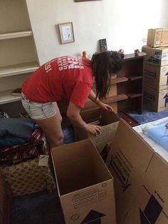 a woman in red shirt packing boxes on floor