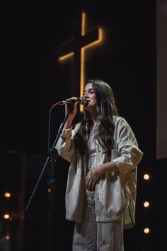 a woman singing into a microphone in front of a cross