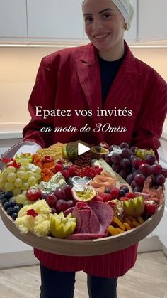 a woman in a red coat holding a platter of fruit and veggies