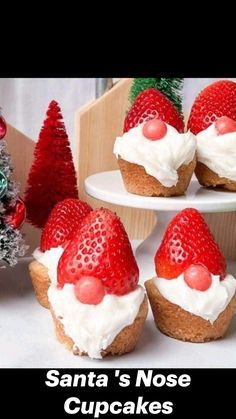 some cupcakes with strawberries on top and christmas trees in the back ground