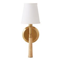 a gold wall light with a white shade on the side and a wooden stick in front of it