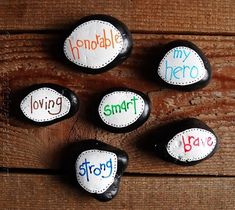 six rocks with words painted on them sitting on a wooden surface