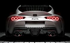 the rear end of a white sports car with its lights turned on in the dark