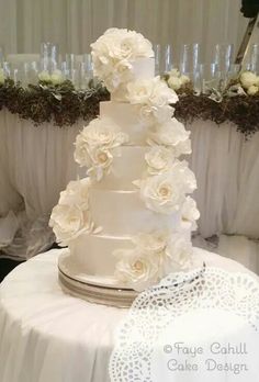 a wedding cake with white flowers on it sitting on a table in front of wine glasses