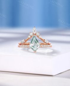 an engagement ring with a green and white stone surrounded by small diamonds on a table