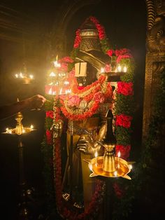 a statue with candles and flowers around it in front of a light filled wall that is lit up