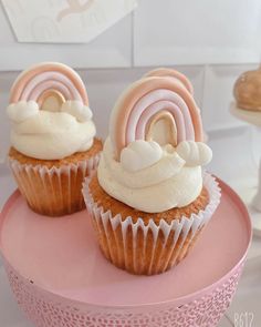 two cupcakes with white frosting and pink icing on a pink plate