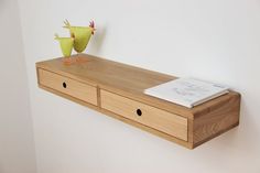 a wooden shelf with two drawers and a paper bird on it's head, against a white wall