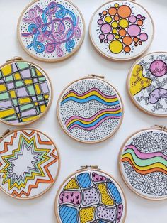 embroidery designs are displayed on wooden hoops with colored lines and shapes painted on them