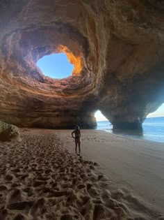 a man standing on top of a sandy beach under a cave