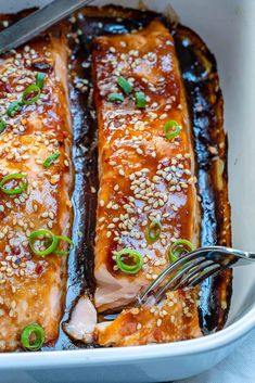 salmon with sesame seeds and green onions in a white casserole dish, being served with a fork