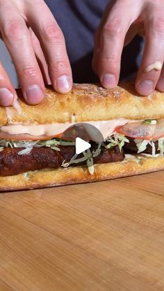 a person is making a sandwich with meat and cheese on a wooden table, while another hand reaches for it