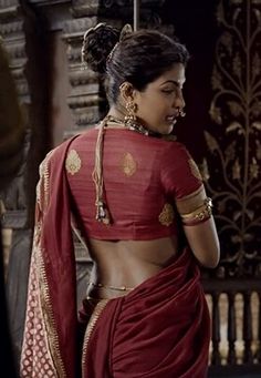 a woman in a red sari with gold accents on her chest and arms, looking to the side