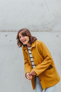 a woman laughing while standing in front of a concrete wall with her hand on her hip