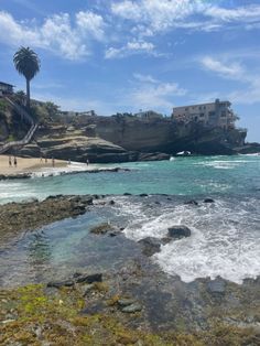 people are walking on the beach next to the water and cliffs with buildings in the background