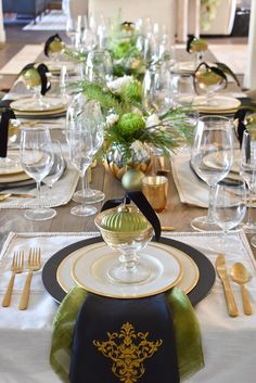 the table is set with gold and black plates, silverware, and green napkins