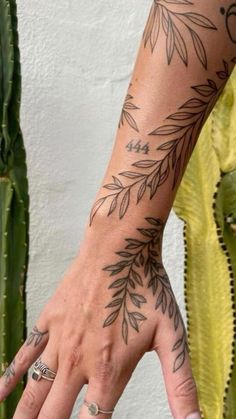 a woman's hand with tattoos on it and a cactus in the back ground