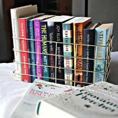 a stack of books sitting on top of a bed next to a book rack filled with books