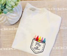 Embroidered Personalized Teacher Crayon Pocket Tee. Perfect for teacher appreciation or birthday gifts! These are comfort colors tees. Relaxed fit. White School Spirit T-shirt With Embroidered Graphics, White Embroidered School Spirit T-shirt, White T-shirt With Embroidered School Spirit Graphics, White T-shirt With Embroidered Graphics For School Spirit, Casual School T-shirt With Embroidered Graphics, School T-shirt With Embroidered Text And Crew Neck, School Spirit Cotton T-shirt For Gift, School T-shirt With Embroidered Crew Neck, Cotton School Spirit T-shirt As Gift