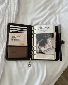 an open leather wallet sitting on top of a bed next to a notepad and pen