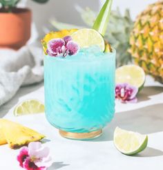 there is a blue drink with lemons and flowers on the table