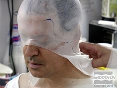 a man wearing a white mask and covering his face with a piece of paper on top of his head