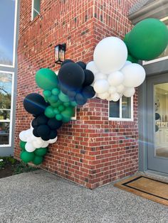 some balloons are hanging from the side of a brick building and it is green, white and black